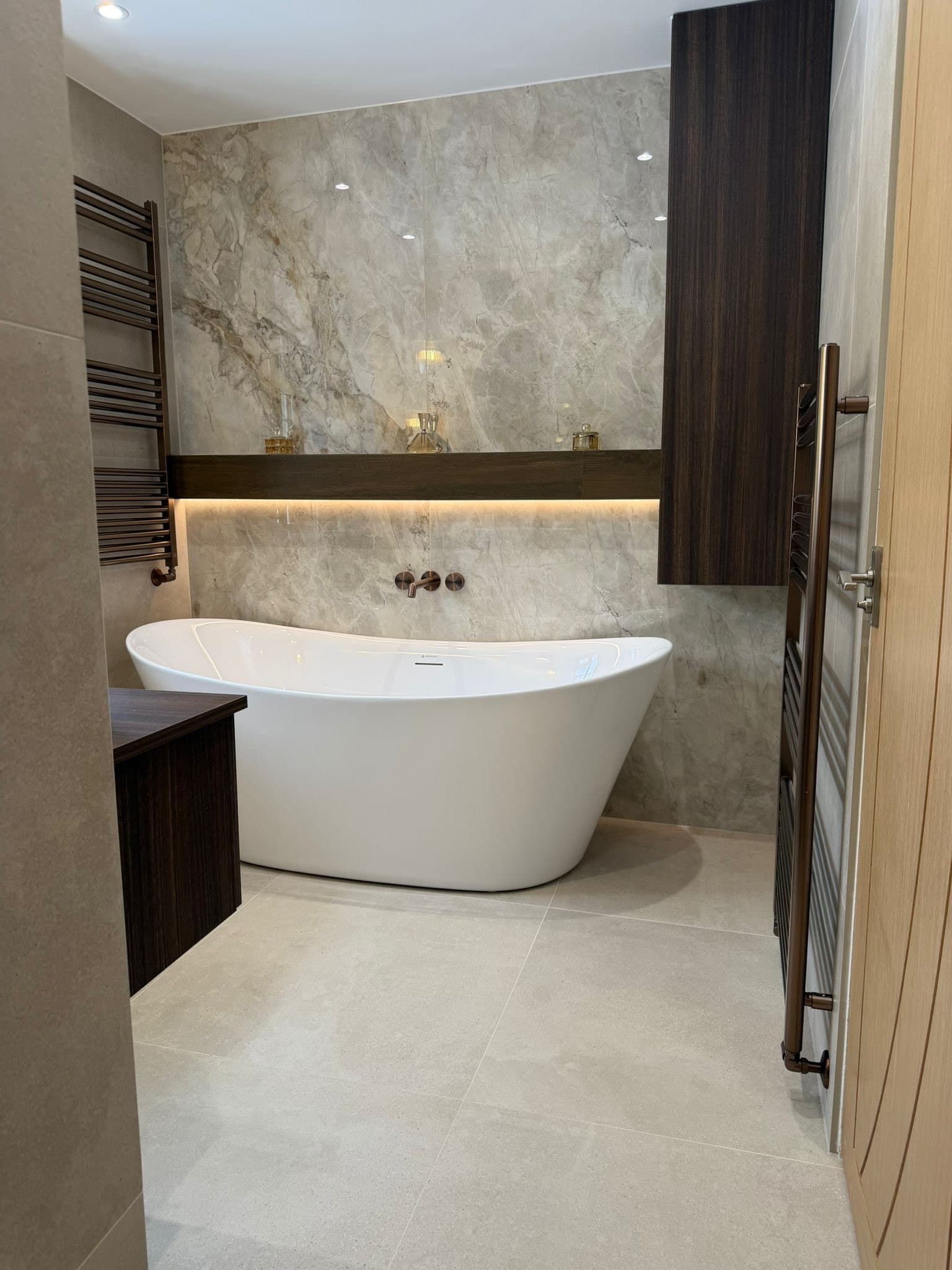 Freestanding bath, tall timber cabinet and warm LED shelf against marble-effect walls