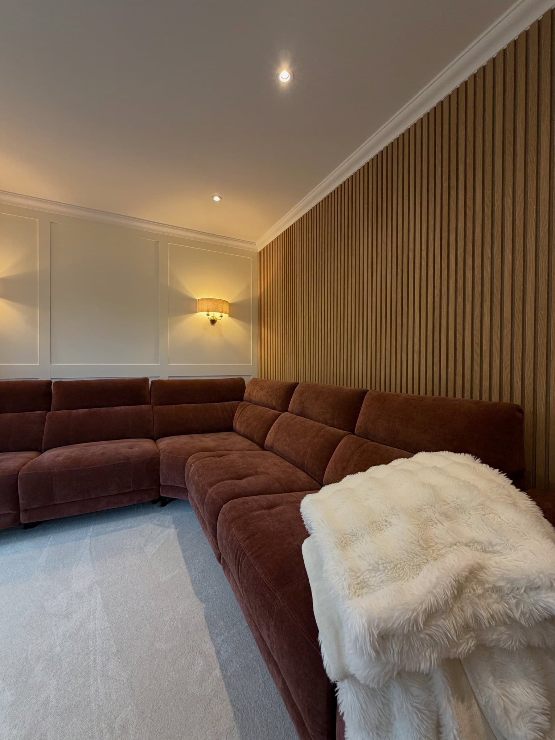 Living room with shaker wall panelling, oak slat feature wall and warm wall lights